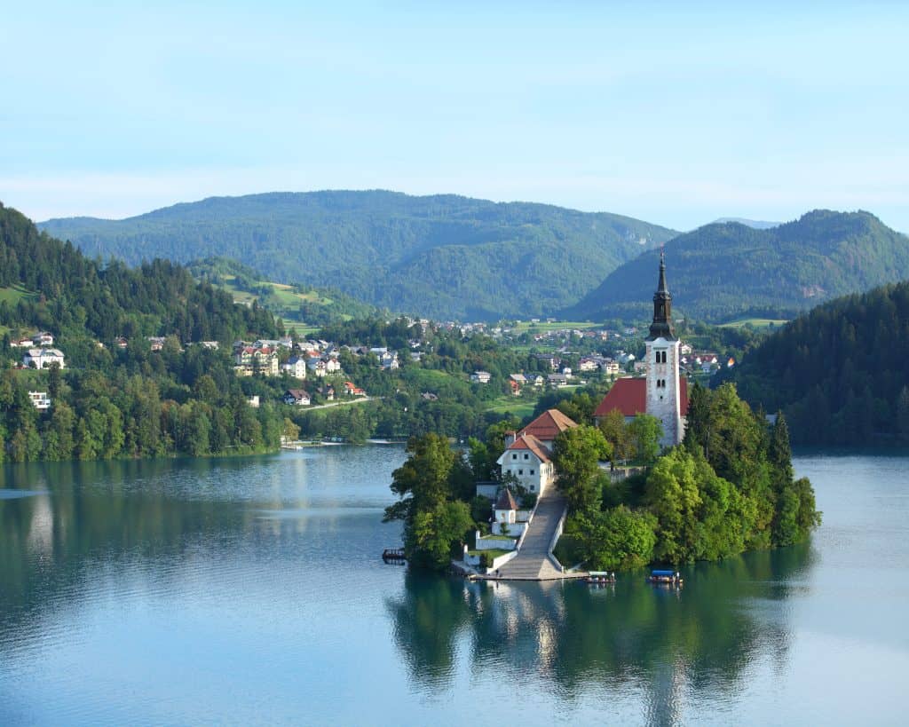 Lake Bled castle in Slovenia - a small isnland on a lake surrounded by mouuntains. Ther eis a caslte peeking out among the trees on the island.