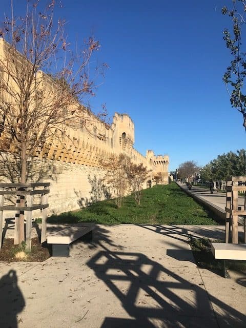 Medieval fortress wall of Avignon with green belt and picnic tables and blue sky.