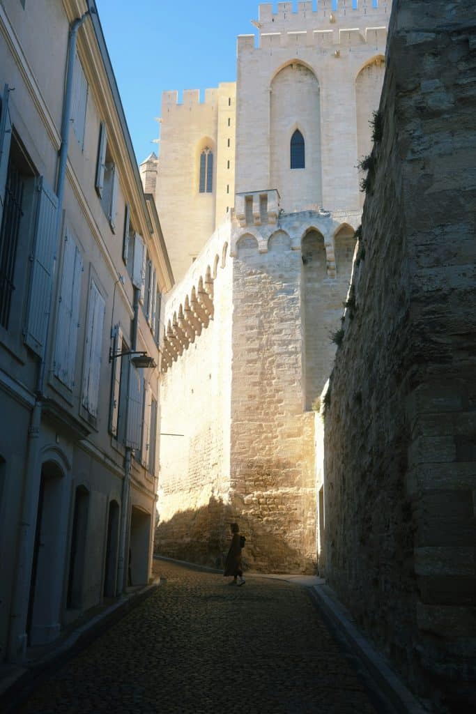 Narrow medieval street in Avignon with very tall ancient building, the pop palance and light streaming in.
